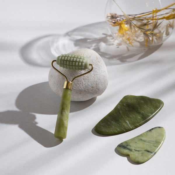 jade face roller and gua sha stones placed against a white stone and white surface background
