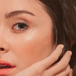 A close up of a woman's face with lash extensions and her hand against her cheek